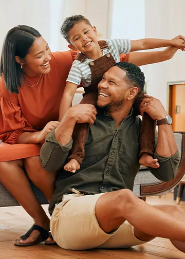  A joyful photo of a family, with the father holding the boy on his shoulders as they all smile.

