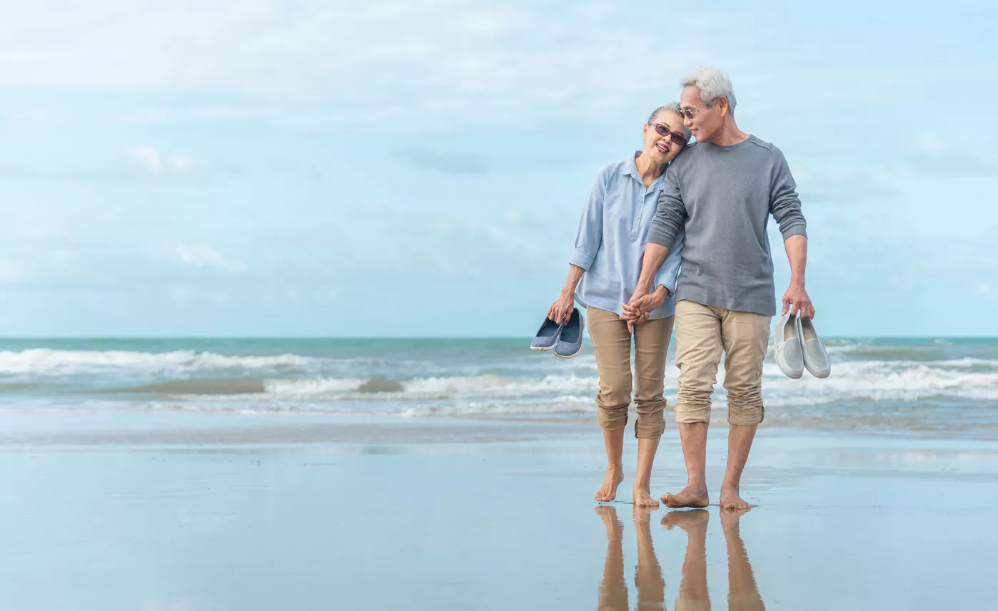  Un couple de personnes âgées se promène le long de la plage en se tenant la main.
