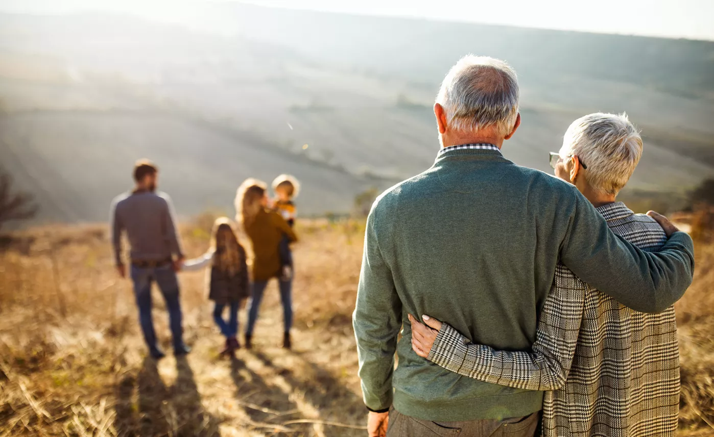  A mature couple watching their children and grandchildren as they all walk through a field.
