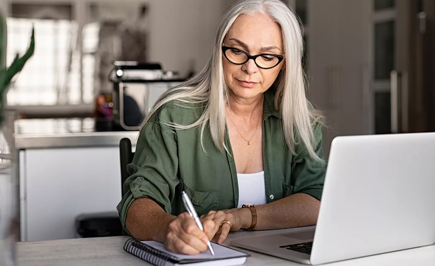  Une femme à l’âge de la retraite prend des notes en utilisant son ordinateur portable.
