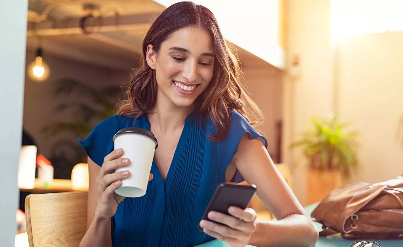  Une jeune femme examine son compte sur un téléphone mobile en prenant son café.
