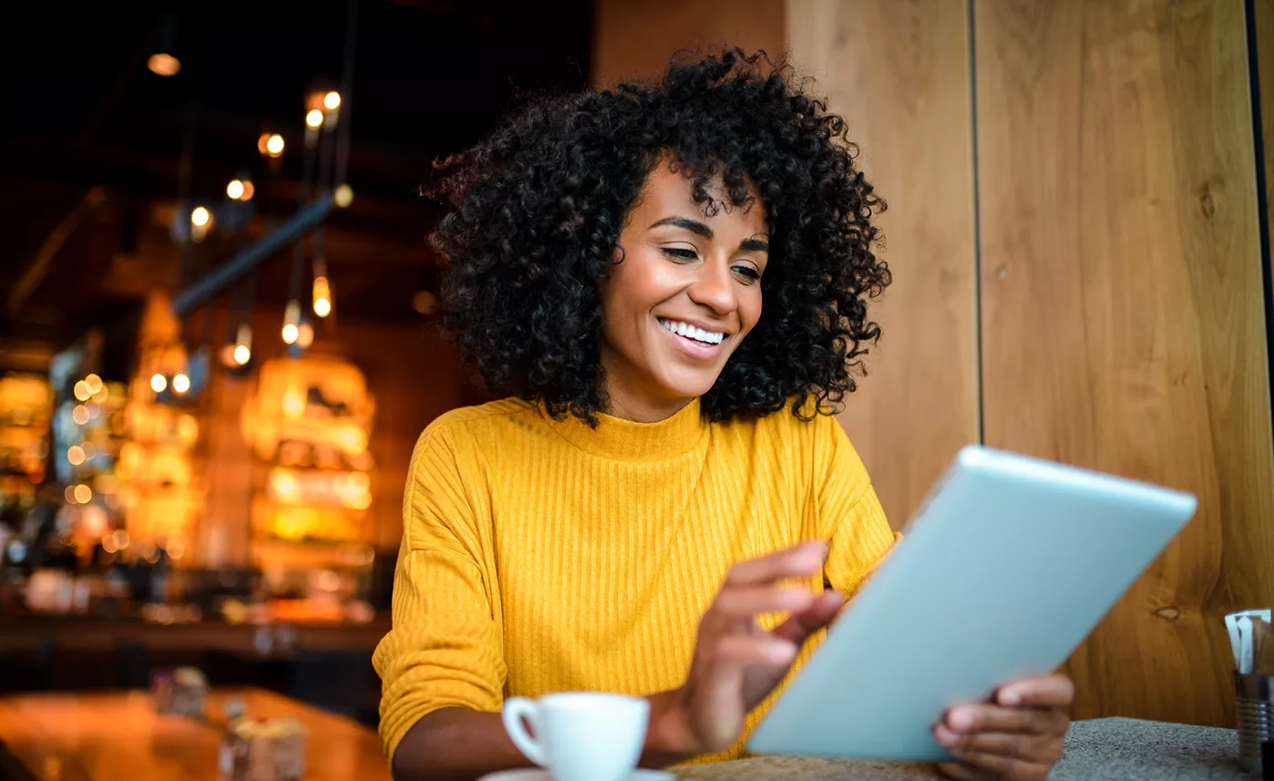  A millennial woman smiles as she reads information on a tablet in trendy cafe.
