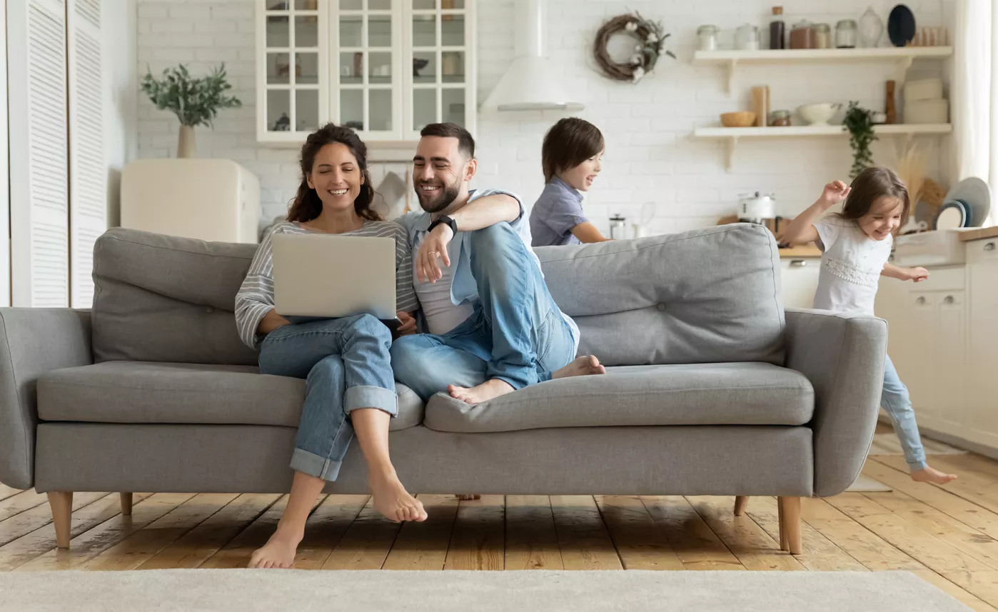  Two parents sit on the couch and check their Edward Jones account on a laptop while two children play in the living room.
