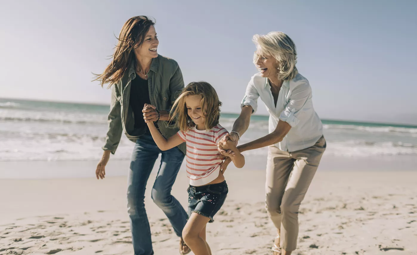  Une retraitée rit sur la plage avec sa fille adulte et sa petite-fille.

