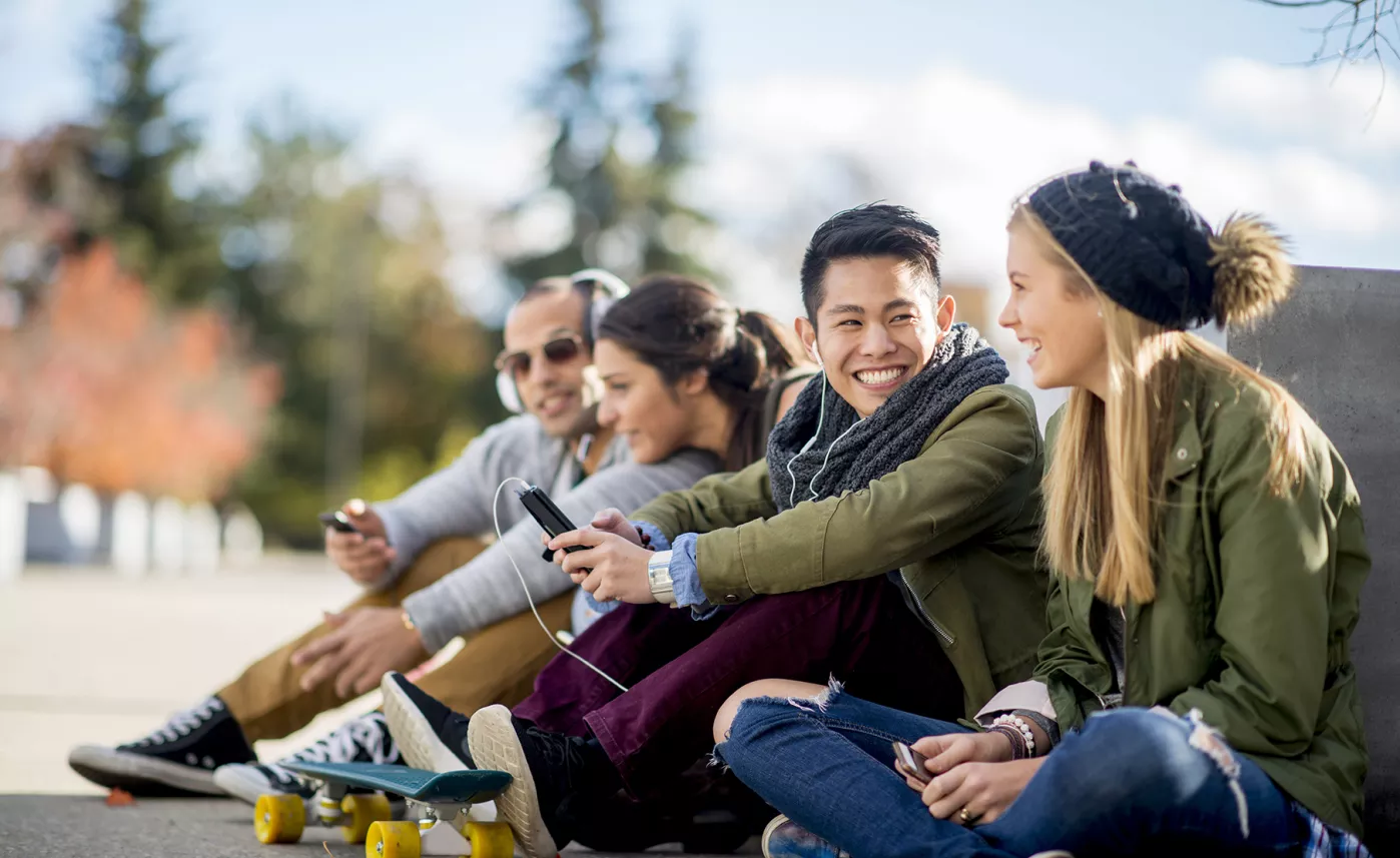  Quatre étudiants universitairessont assis dans un parc et rigolent ensemble.
