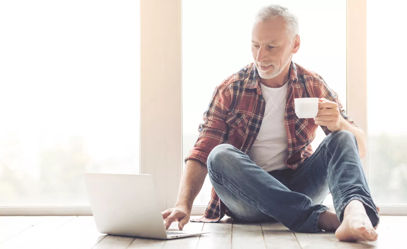  Un homme assis par terre passe en revue des documents financiers en ligne sur son ordinateur portable.
