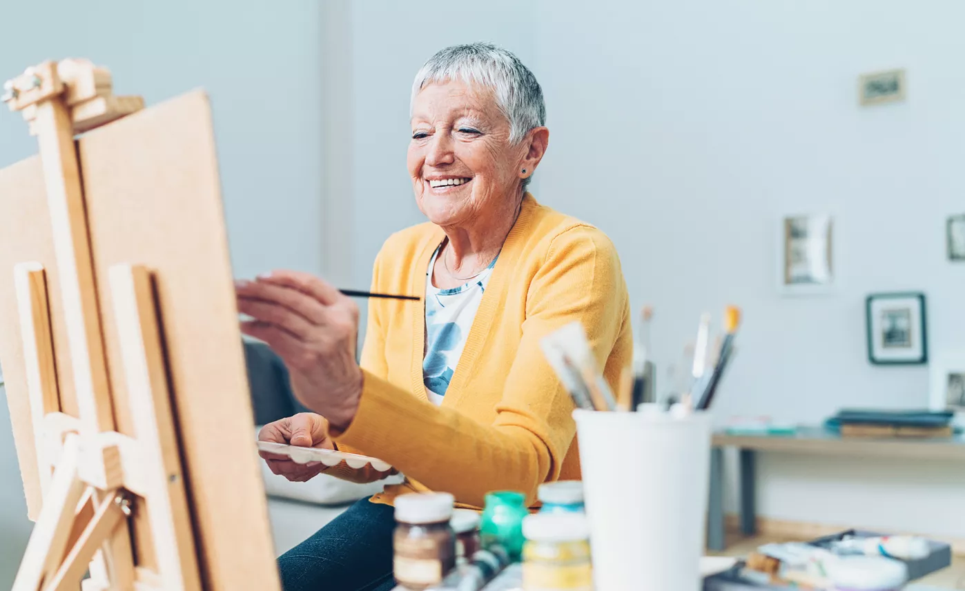  A retirement-aged woman smiles as she paints in her home studio, enjoying retirement.
