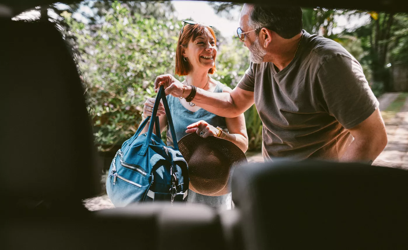 A couple taking their luggage out of a car.