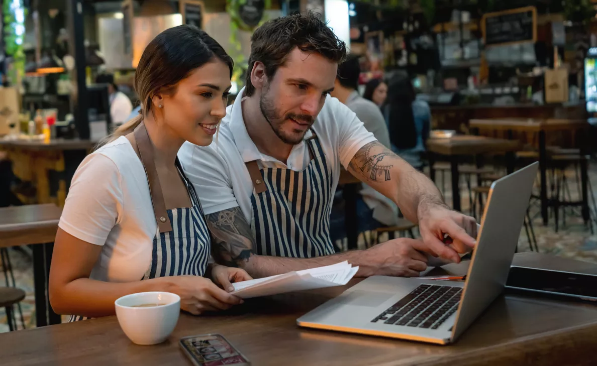  A couple of young professional small business owners reviews information on their laptop in their trendy cafe.
