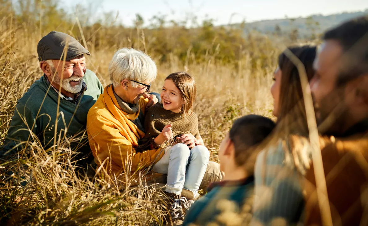 An adult woman joyfully playing with her young granddaughter in a sunlit field, surrounded by tall grass and wildflowers, capturing a moment of warmth and connection.