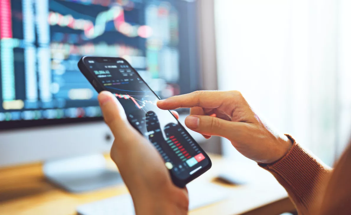 Hands using a smartphone stock‑trading app with charts displayed.