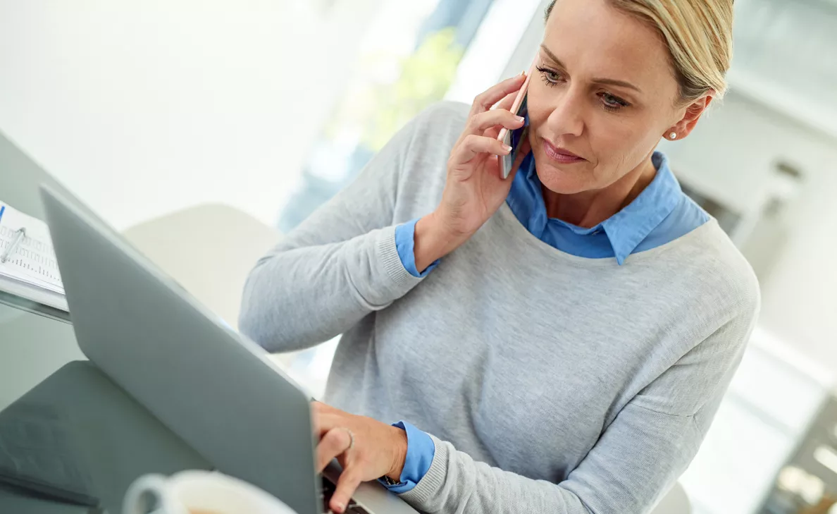 A woman types on her laptop while on a telephone call.