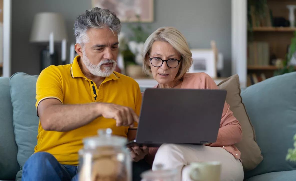  Couple sitting on couch looking at laptop screen.
