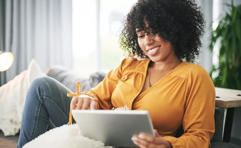 Une femme sourit en lisant de l’information financière sur une tablette dans son salonUne femme sourit en lisant de l’information financière sur une tablette dans son salon.