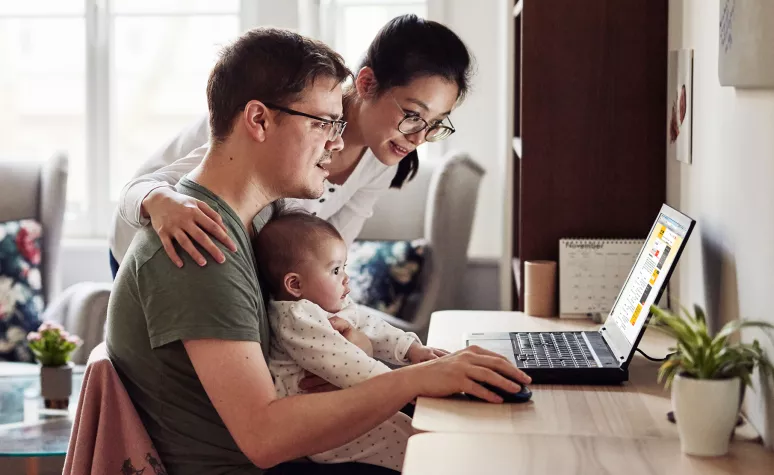 De jeunes parents cherchent des renseignements sur leur ordinateur portable tandis qu’un petit bébé se trouve sur les genoux du père.