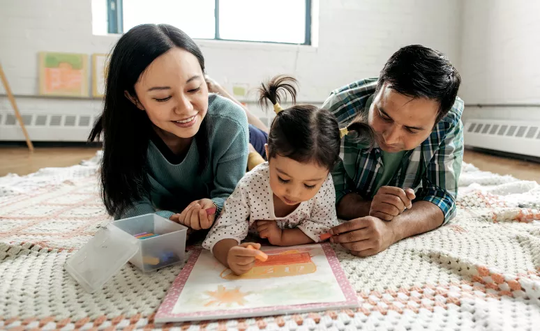 Young parents sit with their toddler daughter as she colors. Young parents sit with their toddler daughter as she colors.
