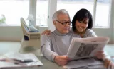 Une femme lit le journal en compagnie de son père âgé.