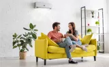 A young couple sit on a bright yellow couch and discuss retirement in a trendy minimalist apartment.