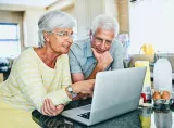 A retirement-aged couple review their finances on a laptop.