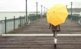 A young woman walks down a pier holding an umbrella on a rainy day.