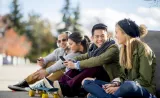 Quatre étudiants universitaires sont assis dans un parc et rigolent ensemble.