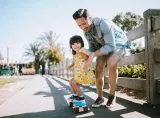 A father holding her daughter standing on a roller skating board