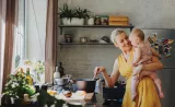 Woman holding and smiling at her baby in her kitchen at the stove while stirring a pot of food
