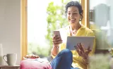 Une personne assise dans une fenêtre, regardant une tablette.