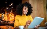 A woman smiles as she reads information on a tablet in trendy cafe.
