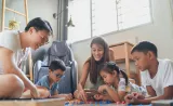 Des parents jouent à un jeu de société sur le sol avec trois jeunes enfants.
