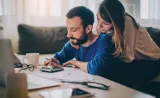 A couple looking at a calculator surrounded by paperwork.