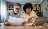 Un couple examine des documents papier ensemble tout en regardant une tablette.